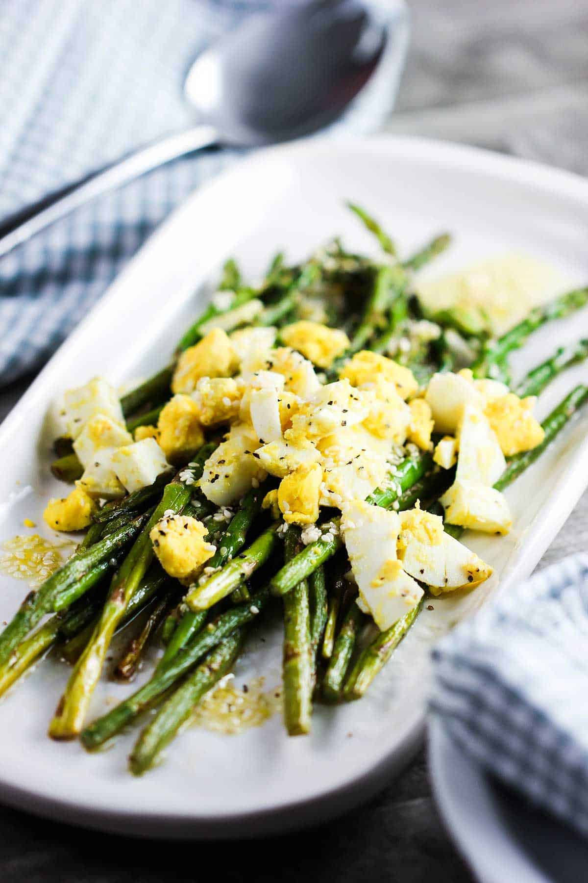 A white platter filled with roasted asparagus with chopped egg on top. 