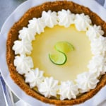 A key lime pie with a graham cracker crust and whipped cream pinwheels along the edges of the top of the pie.