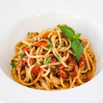 A white pasta bowl with a wide lip is filled with a serving of pasta pomodoro.