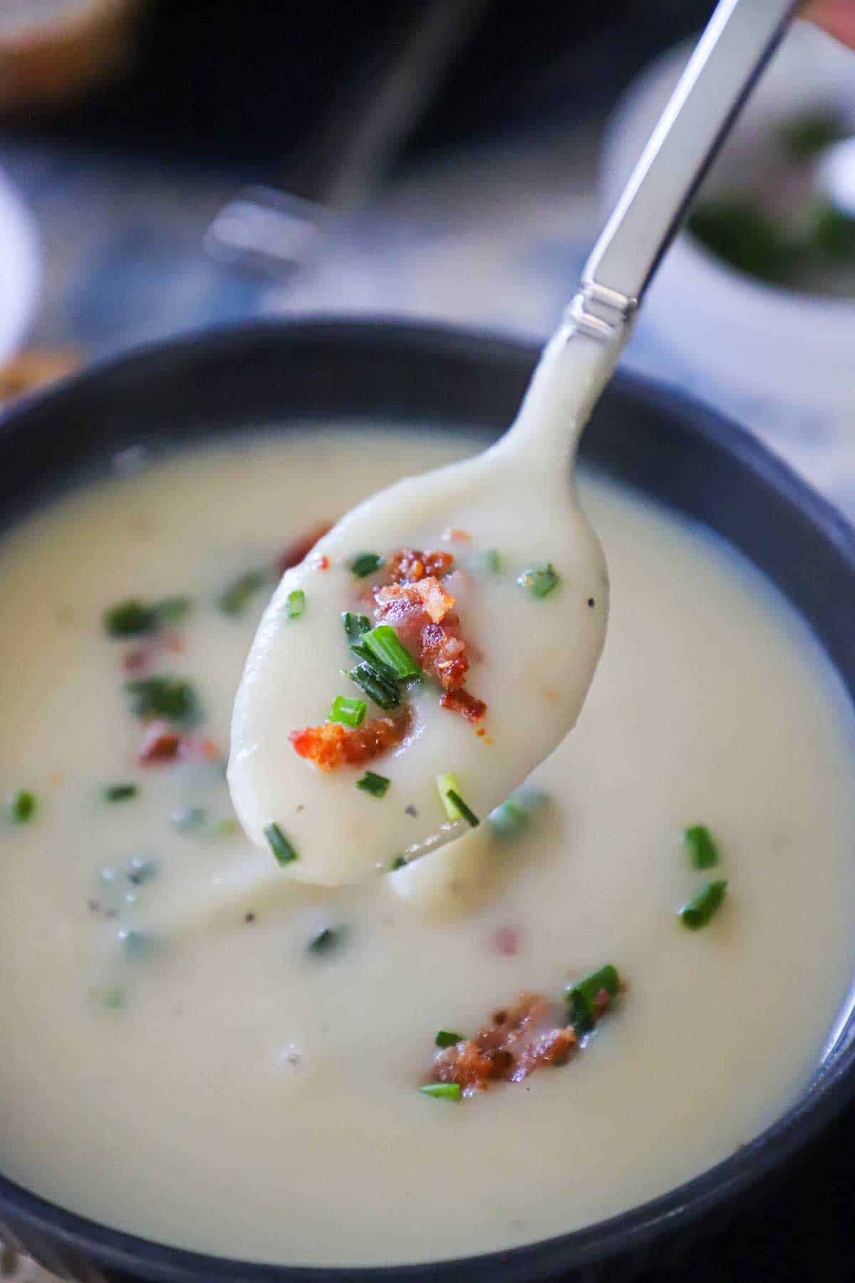 A soup spoon being raised from a bowl of creamy Irish potato soup with bacon and chives on top.