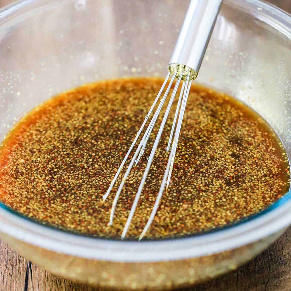 A glass bowl filled with a honey bourbon and ground mustard glaze in it with a whisk inserted in the middle of the bowl.
