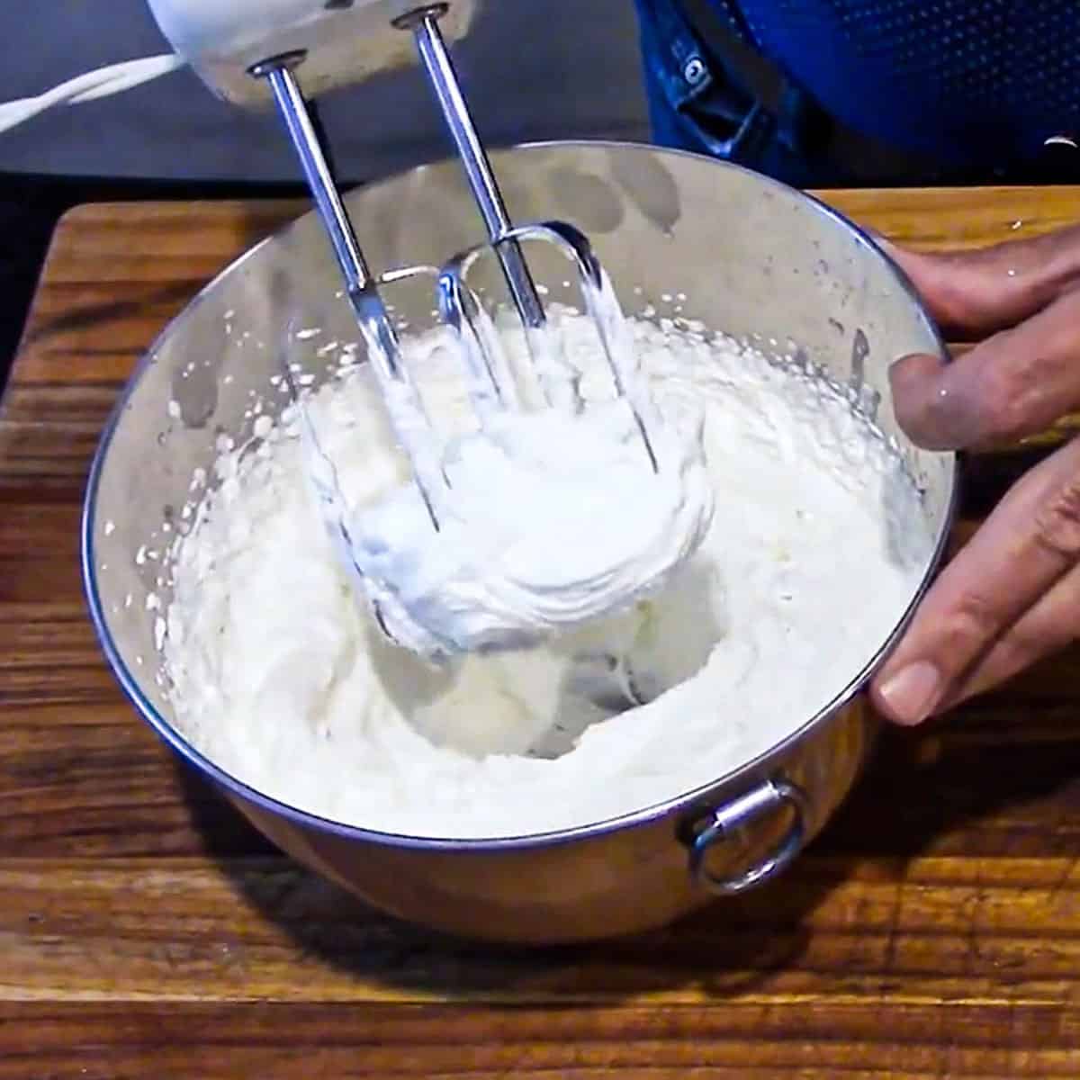 A person using an electric mixer to whip heavy cream into whipped cream.
