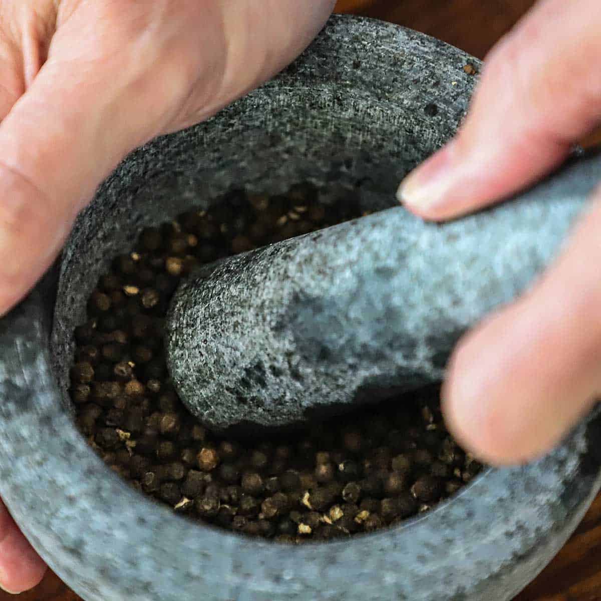 A person using a mortar and pestle to grind toasted black peppercorns.