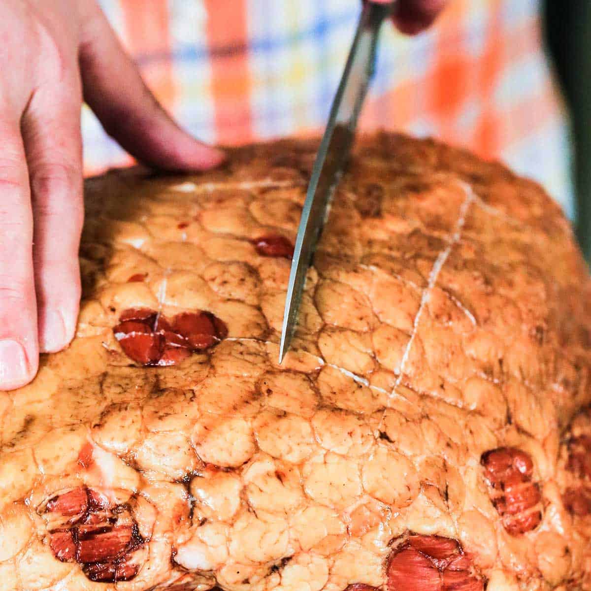 A person using a large chef's knife to score the top of a smoked Berkshire ham.