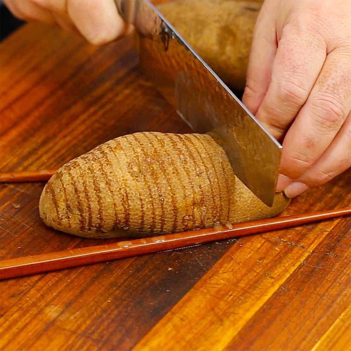 A person cutting slices into a russet potato that is being held in place by two chop sticks.