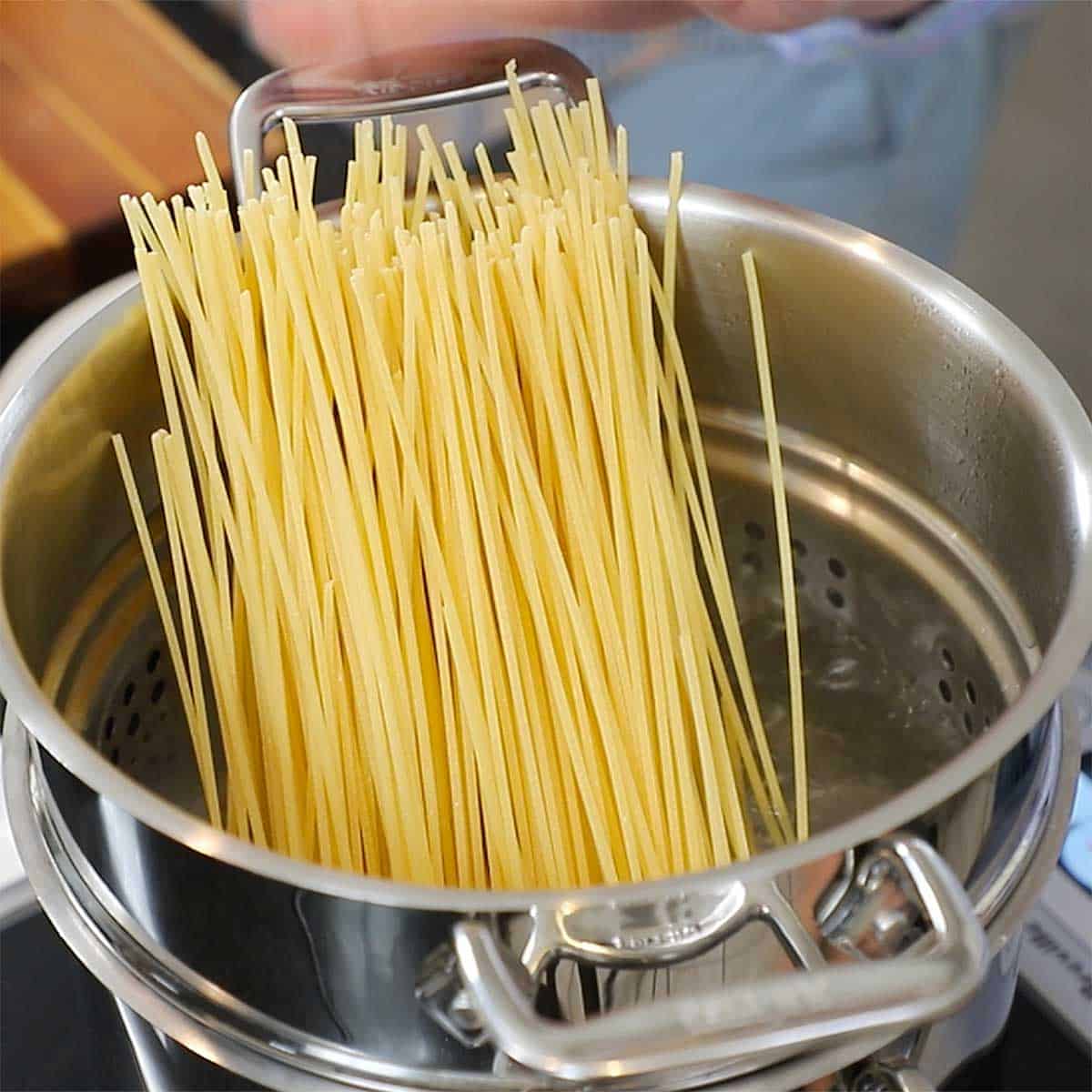 Dried pasta standing upright in a pasta pot filled with boiling water.