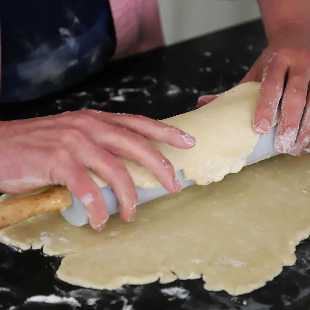A person using his hand to roll pie dough around a marble rolling pin