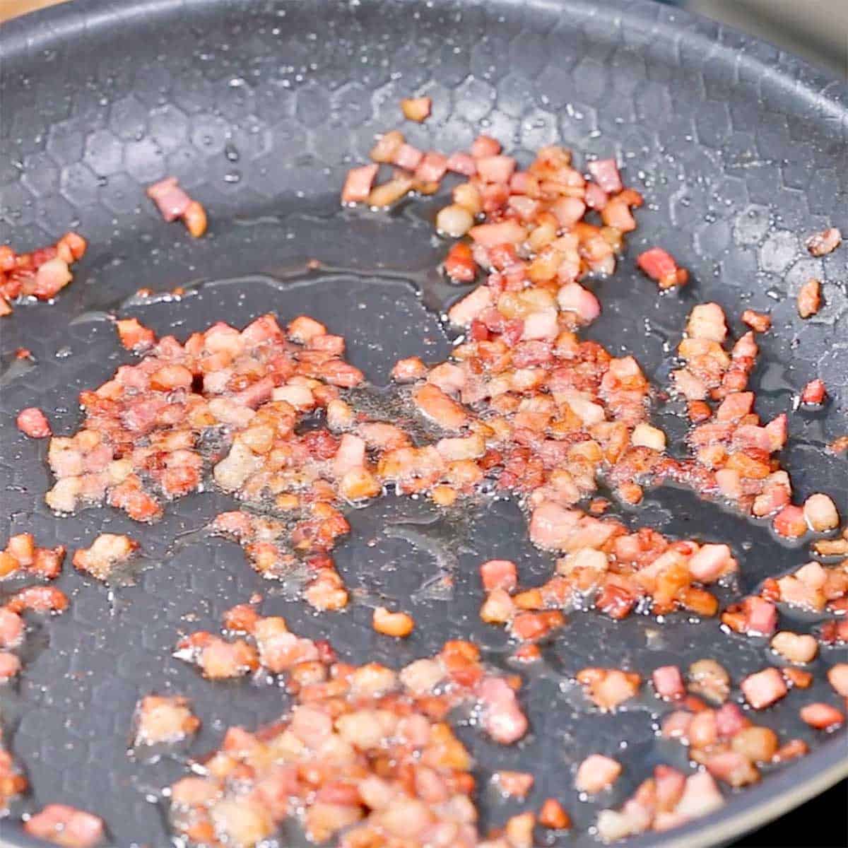 Cubed pancetta being sautéed in a large non-stick skillet.