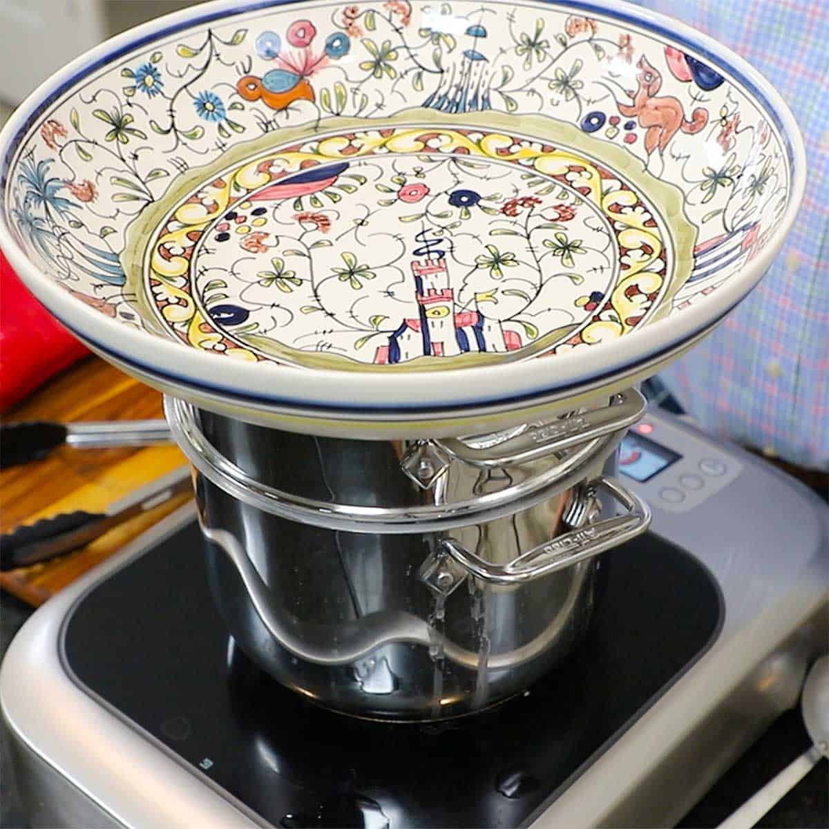 A large colorful pasta bowl resting on top of a paste pot that is sitting on a portable induction stovetop.