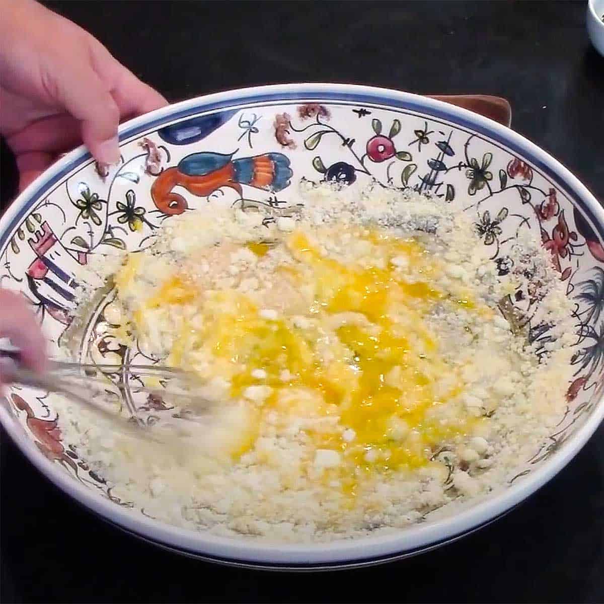 A person whisking egg yolks and grated Romano cheese in a large shallow pasta bowl.