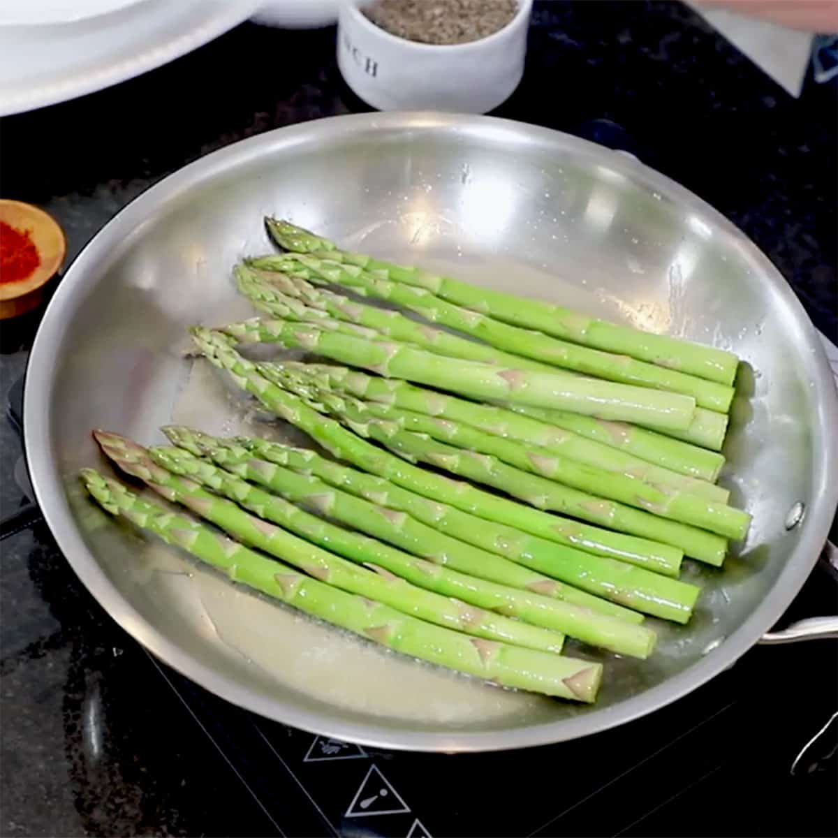 Asparagus being sautéed in melted butter in a large skillet on the stove.