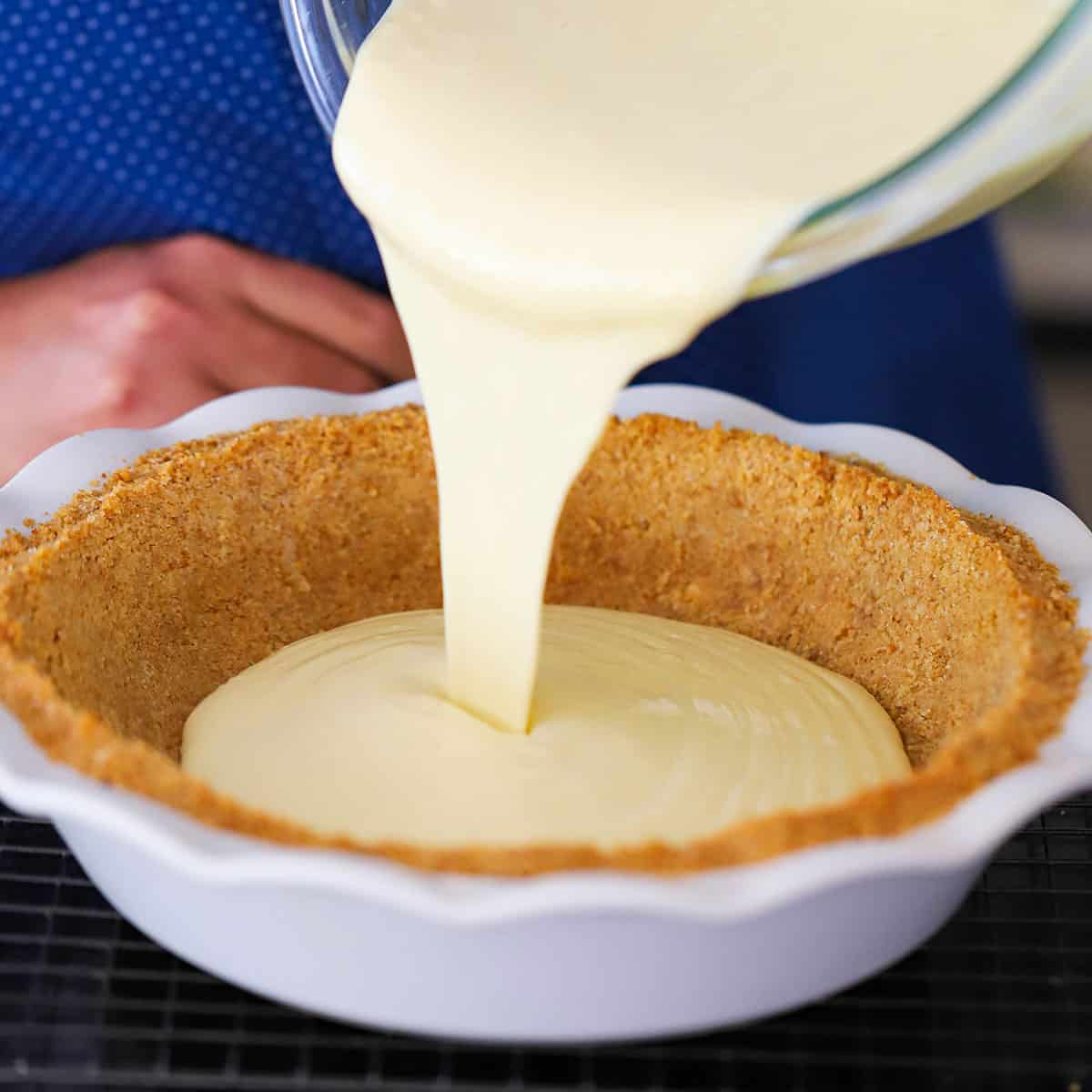A person pouring key pie filling into a pie dish lined with a graham cracker crust.