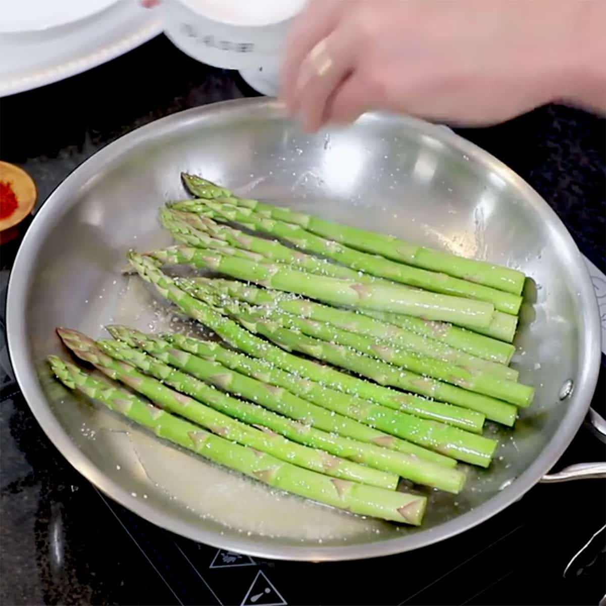 A person sprinkling salt onto asparagus that is being sautéed in a large skillet on the stove.