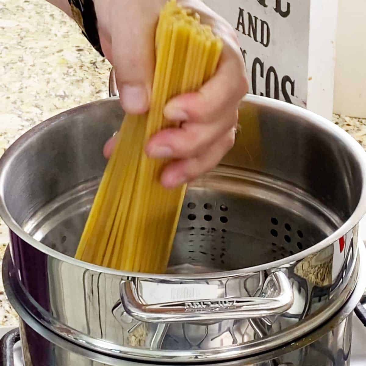 A person placing a bundle of dried bucatini pasta into a pasta pot filled with boiling water.