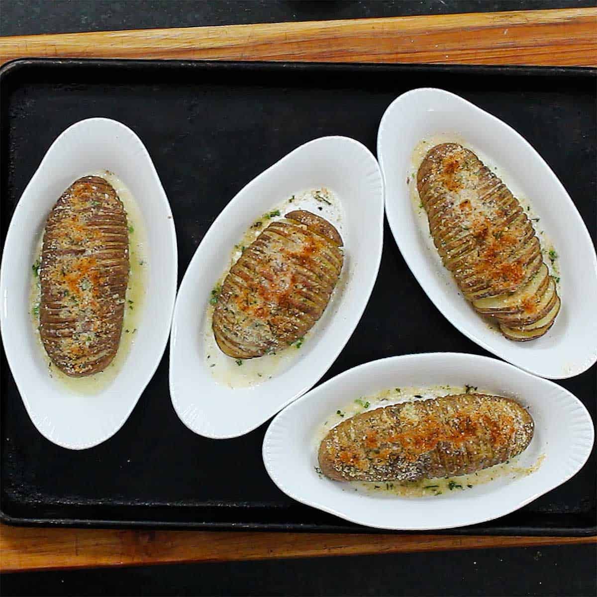 Four hasselback potatoes in their own individual baking dishes that have fully cooked and crispy on top.
