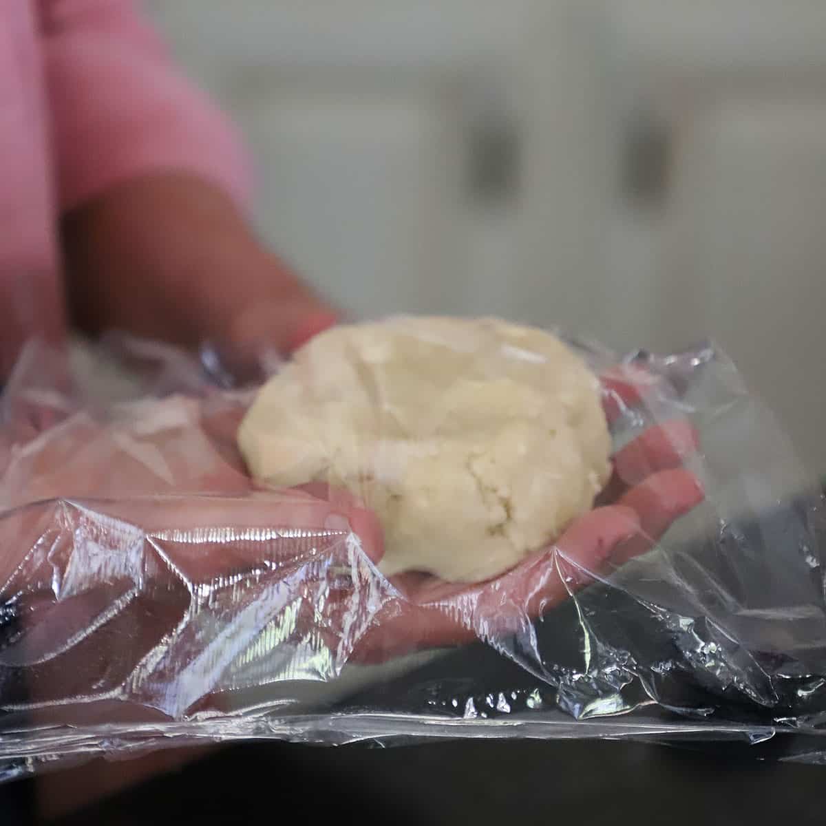 A person wrapping plastic wrap around a disc of easy pie crust dough