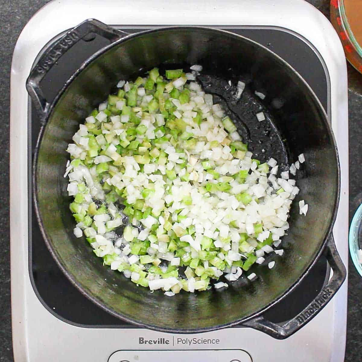Chopped onion and celery being sautéed in butter in a large black pot.