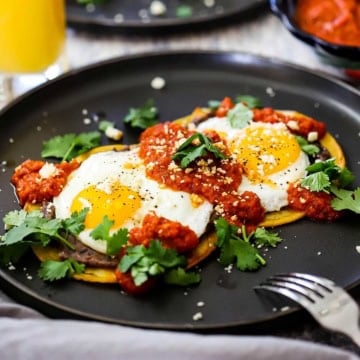 A serving of huevos rancheros on a black plate garnished with crumbled Cotija cheese and chopped fresh cilantro.
