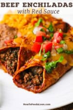 Two beef enchiladas with red sauce on a white dinner plate topped with chopped lettuce and pico de gallo.