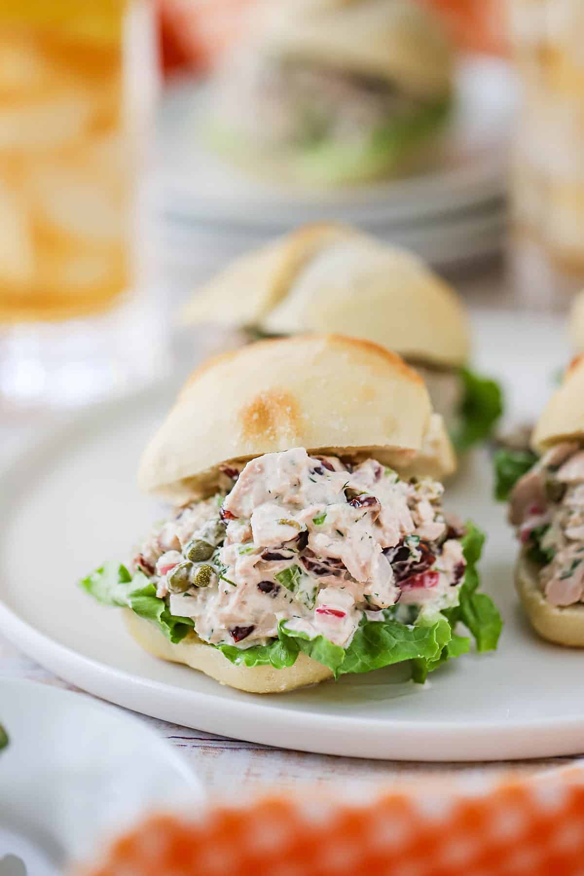 Three tuna salad sandwiches sitting a white lunch plate next to a colorful napkin.