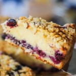 A slice of blueberry almond coffee cake being raised from the cake with metal spatula.