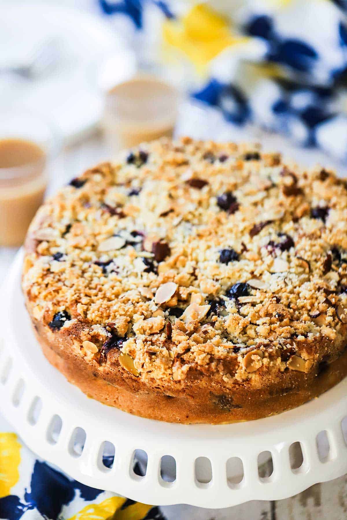 A blueberry almond coffee cake sitting on a white lattice cake stand.