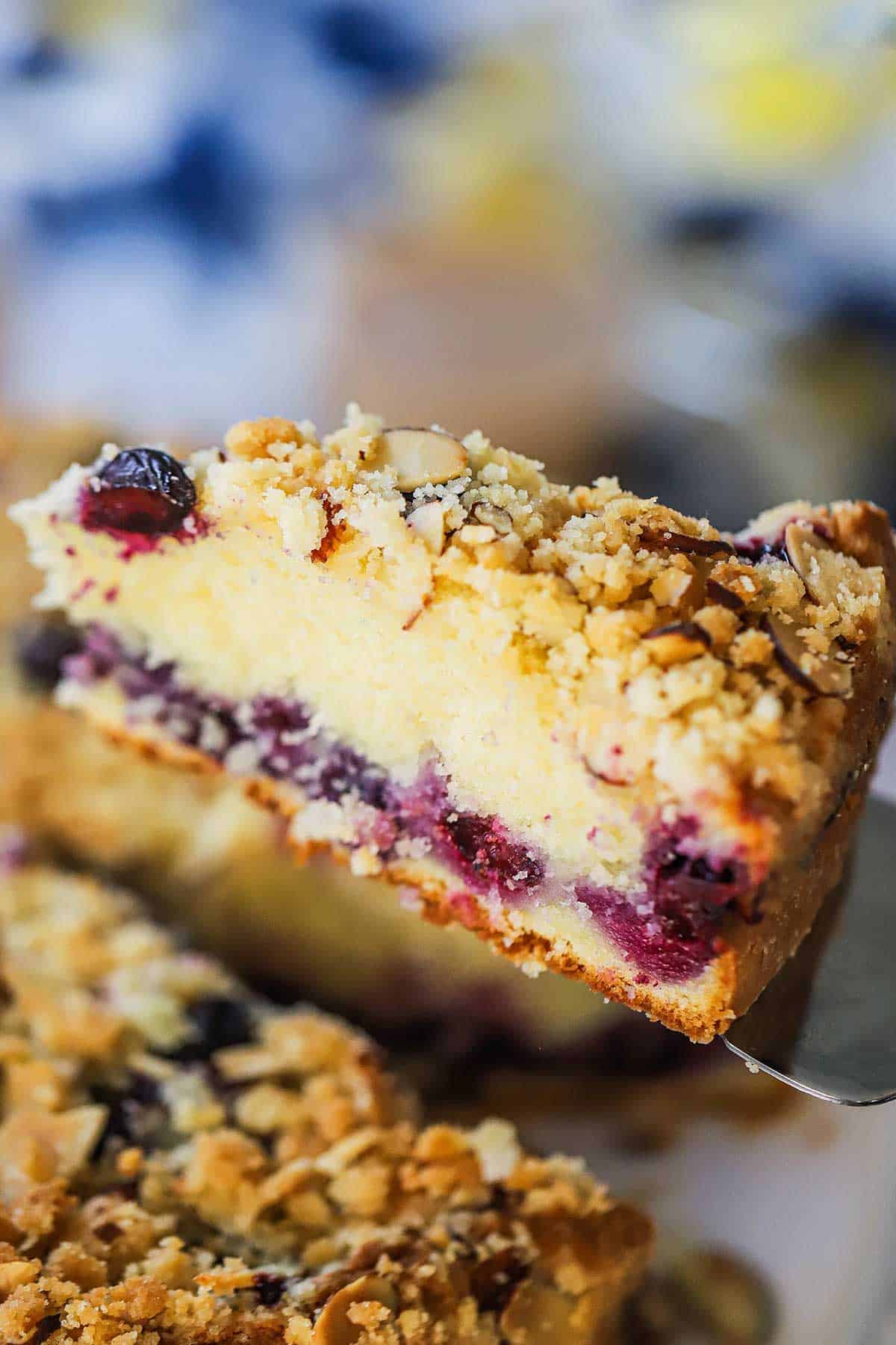 A slice of blueberry almond coffee cake being raised from the cake with metal spatula.