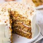 A triple layered carrot cake with a large slice missing from it.