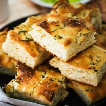 A stack of focaccia with rosemary and olive oil in a bread basket.