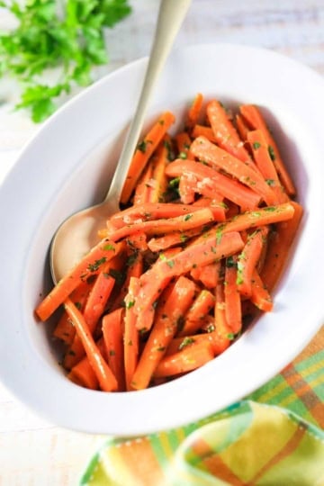 An oval serving dish filled with maple glazed carrots with colorful napkin nearby.