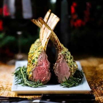 Roast rack of lamb persillade on a white platter with fresh rosemary along the base of the roast.