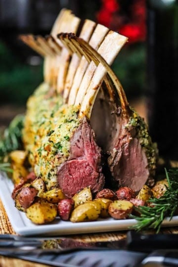 Two racks of lamb persillade standing upright on a white platter with the French bones intersecting each other in a "cathedral" style presentation.