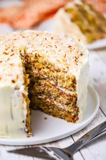 A triple layered carrot cake with a large slice missing from it.