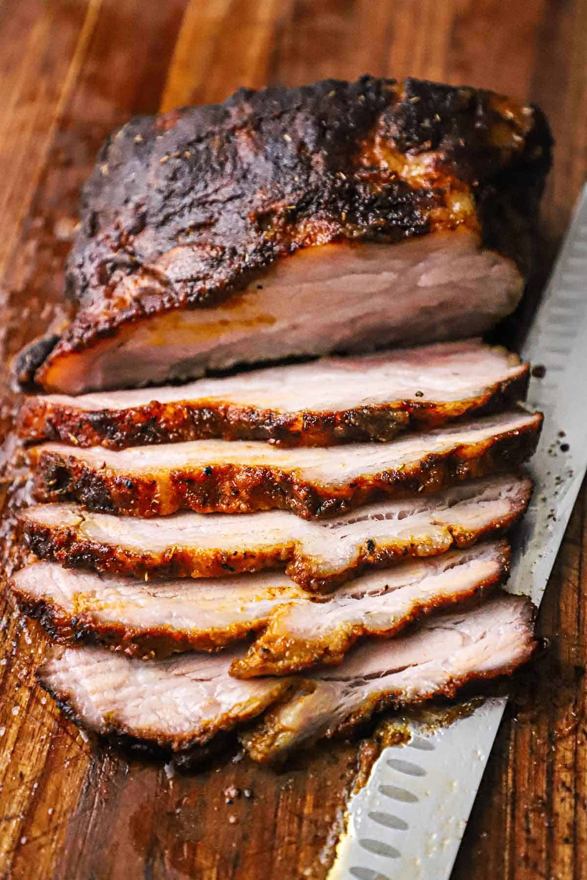 A sliced smoked brisket that is resting on cutting board with a large butcher's knife just underneath the meat.