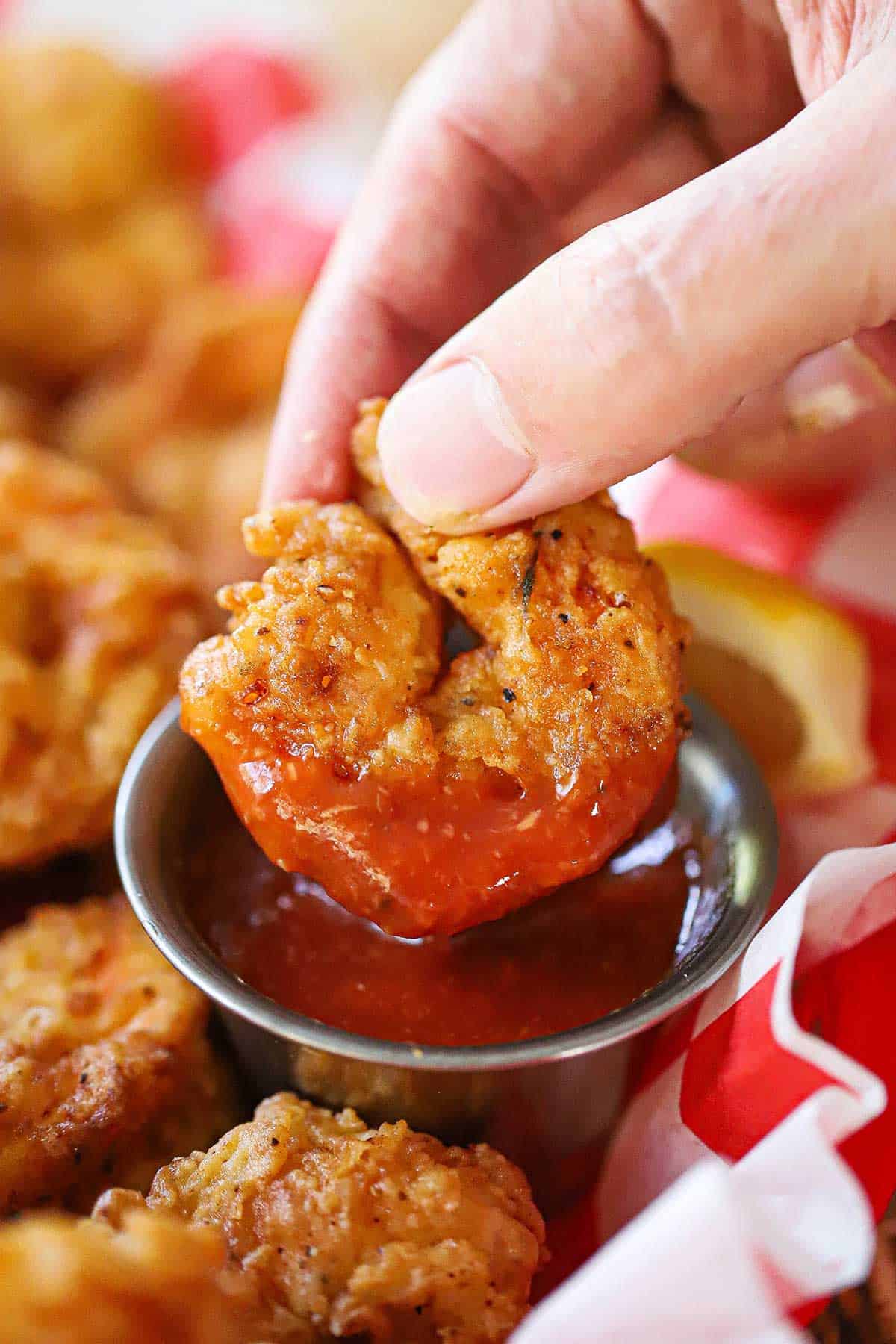 Person using his fingers to raise a Southern-fried shrimp out of a small vessel filled with homemade cocktail sauce.