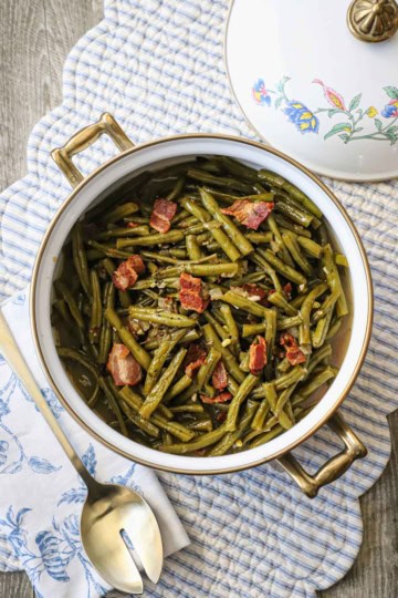 A round pot filled with Southern-style green beans on a white and blue striped place setting.