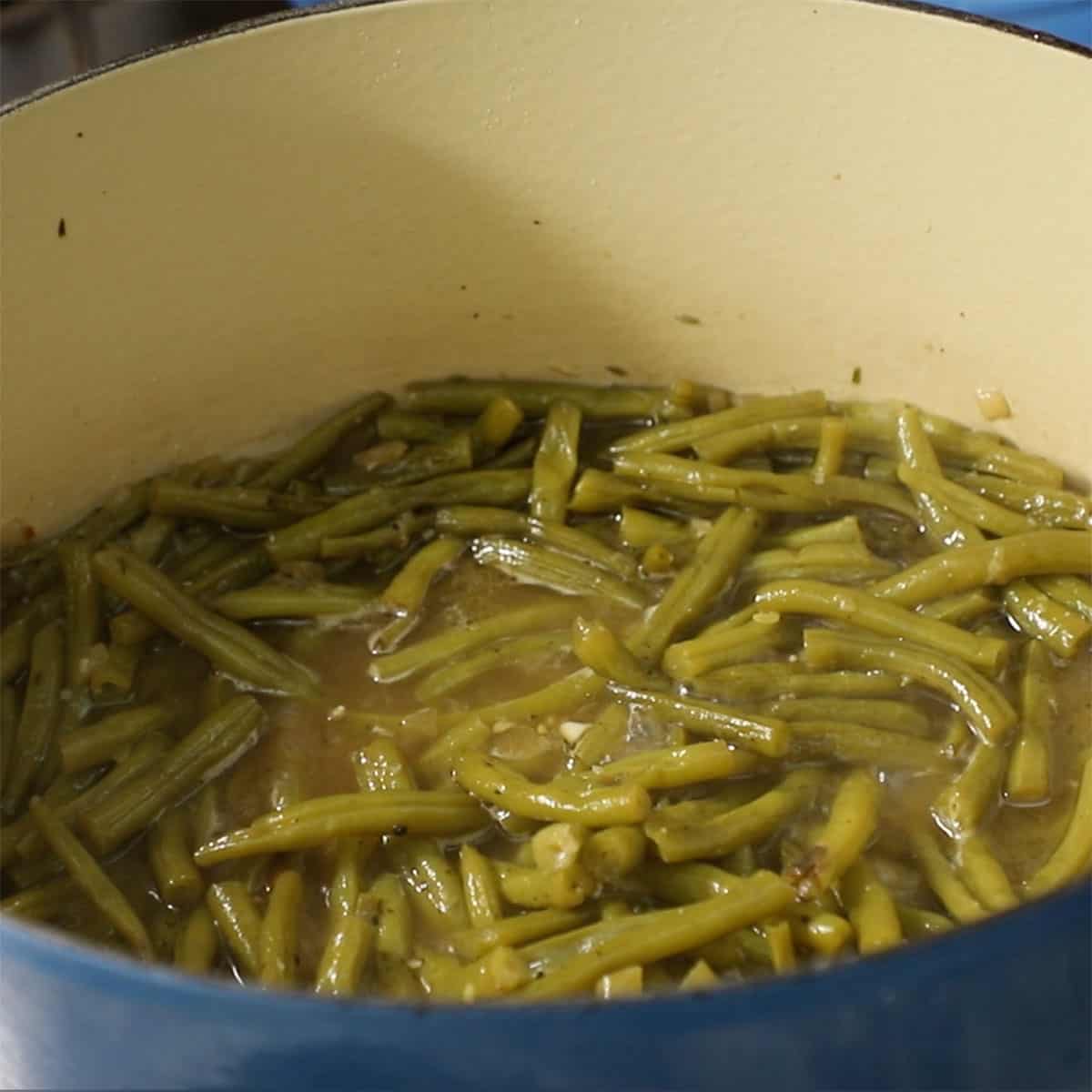 Fresh green beans simmering in chicken broth in a large Dutch oven.