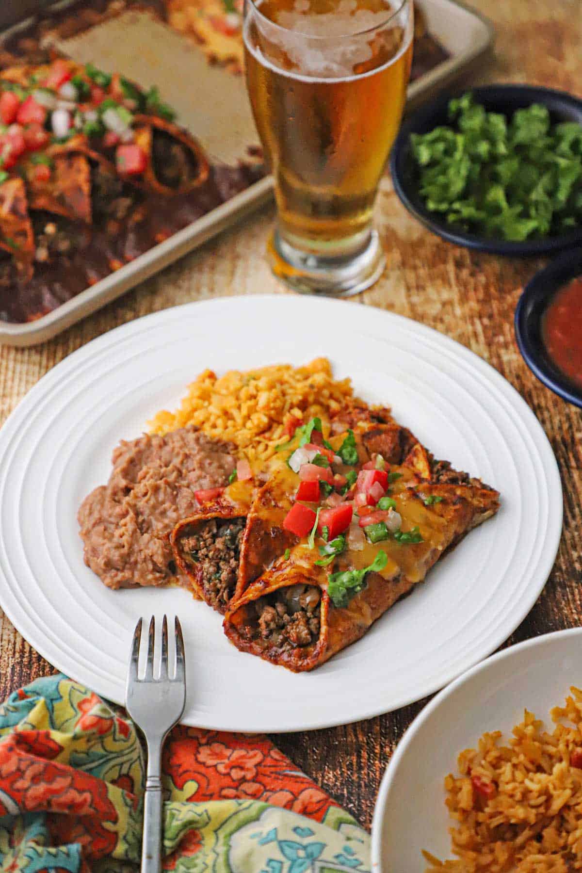 A white plate filled with two beef enchiladas with red sauce next to a serving of Mexican rice and refried beans.