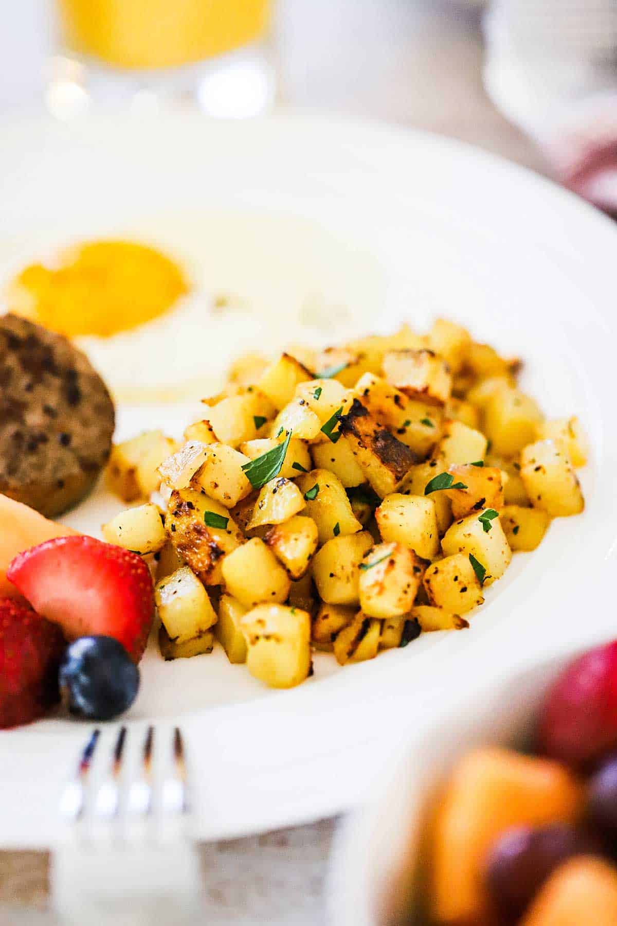 A white plate filled with a serving of breakfast potatoes next to a fried eggs and fresh fruit.