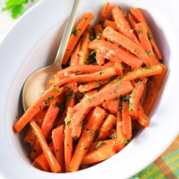 An oval serving dish filled with maple glazed carrots with colorful napkin nearby.