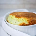 A fully cooked cheese soufflé with cheese in a white dish surrounded by a white linen napkin.