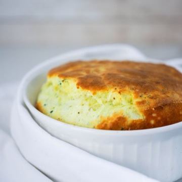 A fully cooked cheese soufflé with cheese in a white dish surrounded by a white linen napkin.
