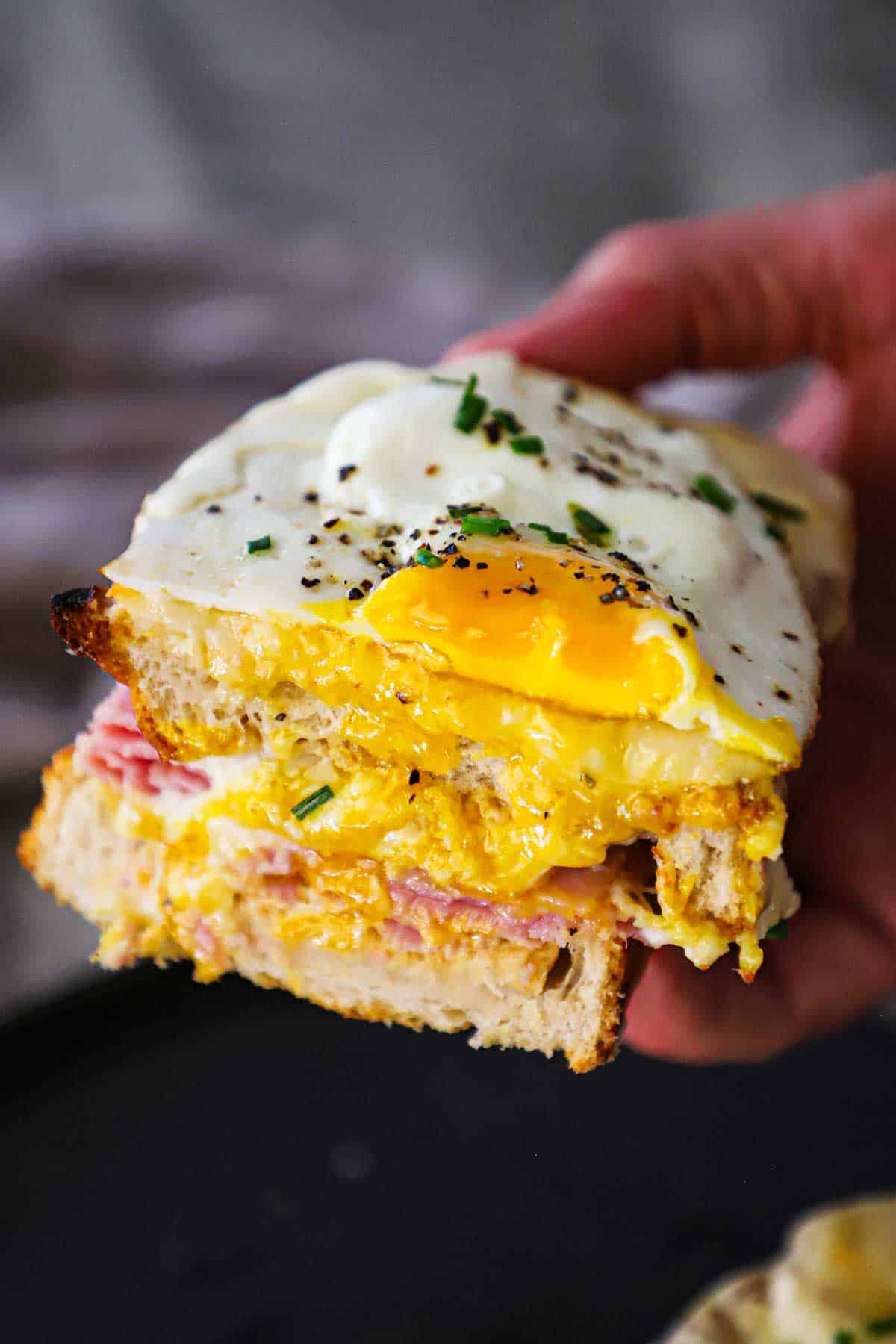 A person holding half of a Croque Madame sandwich in his hand revealing the runny yolk from the egg on top.