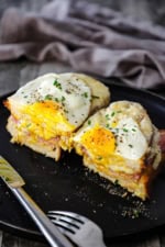 A Croque Madame sandwich that has been split in half on a black dinner plate.
