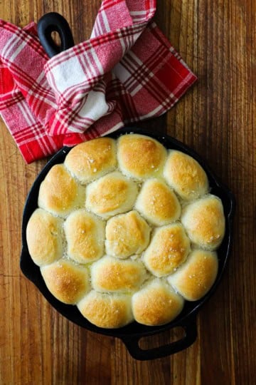 A cast-iron skillet filled with easy skillet dinner rolls with a red checkered napkin wrapped around the handle of the skillet.
