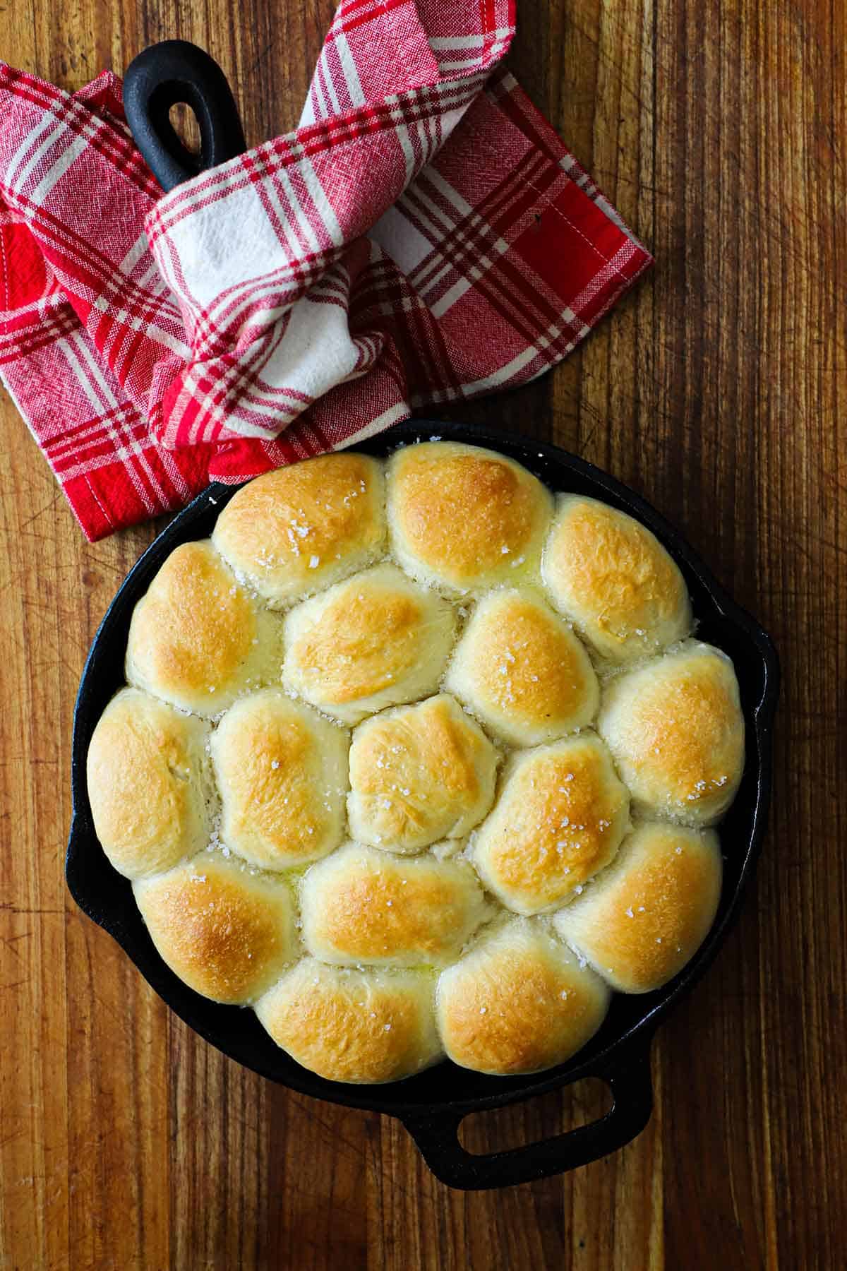 A cast-iron skillet filled with easy skillet dinner rolls with a red checkered napkin wrapped around the handle of the skillet.