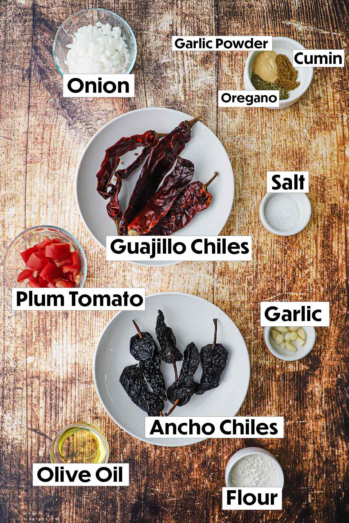 The ingredients for red enchilada sauce arranged on a wooden background, including ripe tomatoes, dried chilies, garlic cloves, chopped onion, and a variety of spices, all neatly organized for easy preparation.