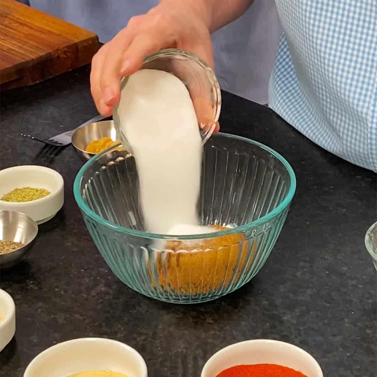 A person pouring granulated sugar into a bowl with brown sugar already in it