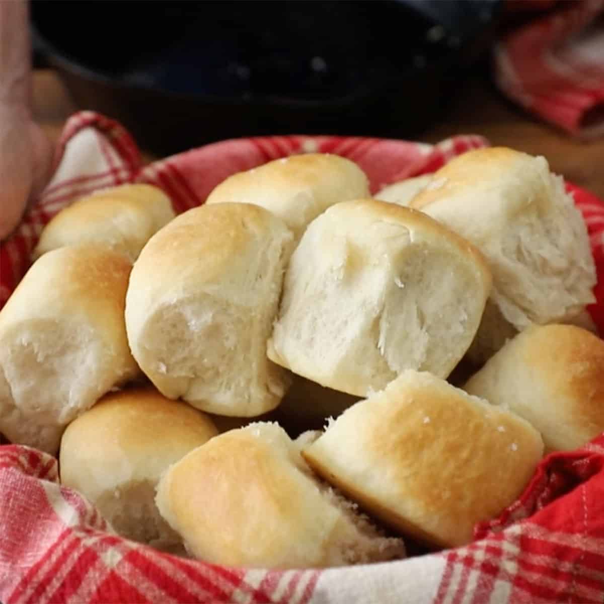 A bread basket lined with a red-checkered napkin and is filled with freshly baked easy skillet dinner rolls.