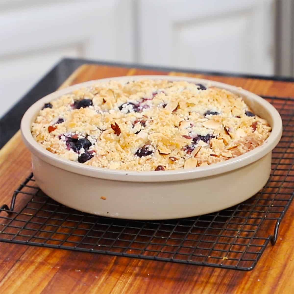 A blueberry almond coffee cake in a cake pan cooling on a baking rack.